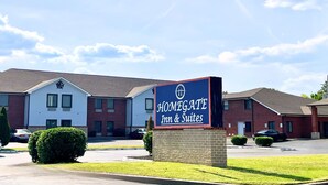 A hotel sign for Homegate Inn & Suites with a brick building and a parking lot in the foreground.
