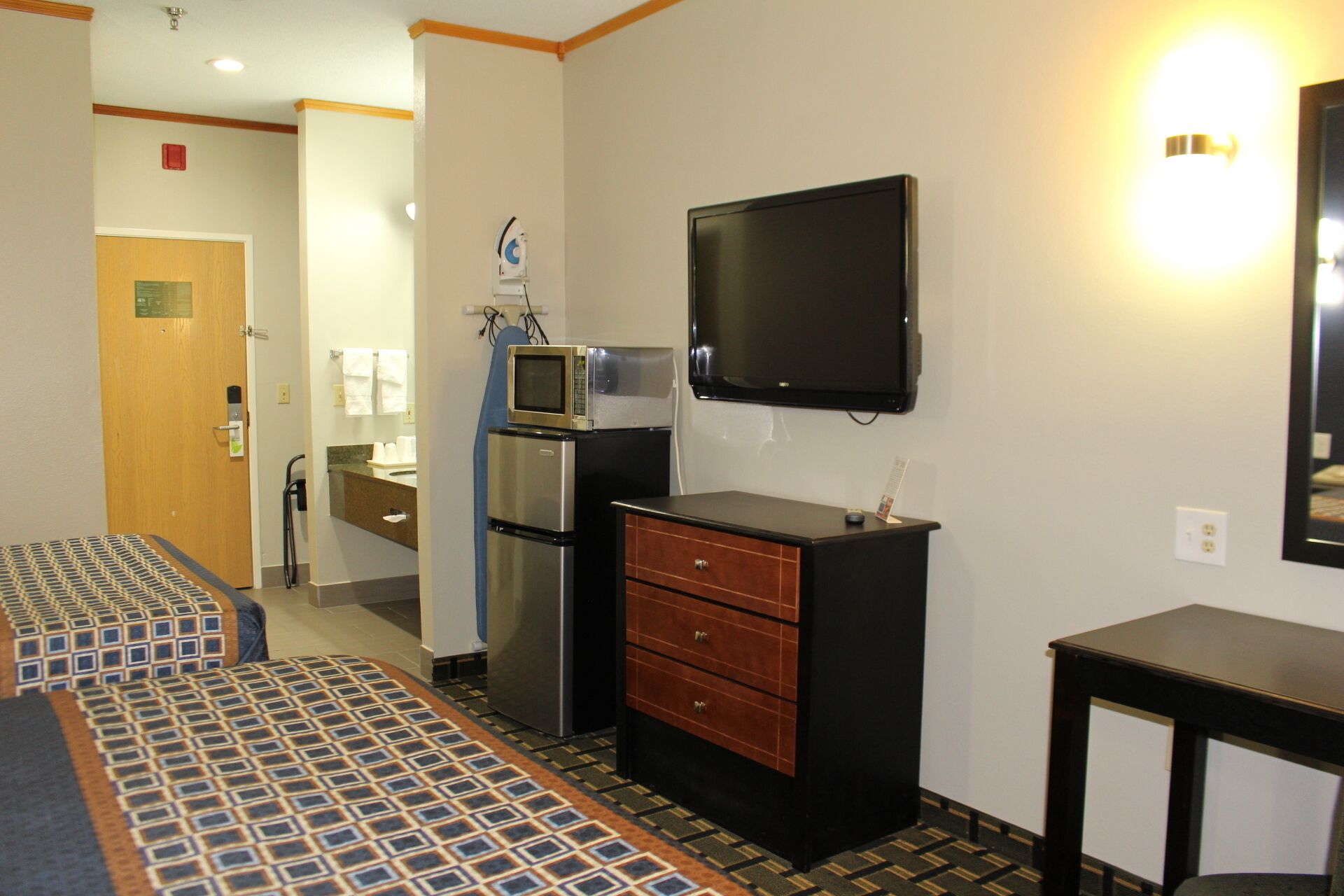 Een hotelkamer met een bed, een minibar, een televisie, een bureau en een badkamer op de achtergrond.