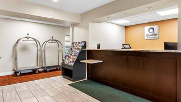 A hotel reception area with a reception desk, a magazine rack, and two wheeled carts.
