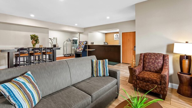 A modern hotel lobby with a grey sofa, a patterned armchair, a reception desk, and a dining area with a table and chairs. - Quality Inn Sawyer (Sawyer)