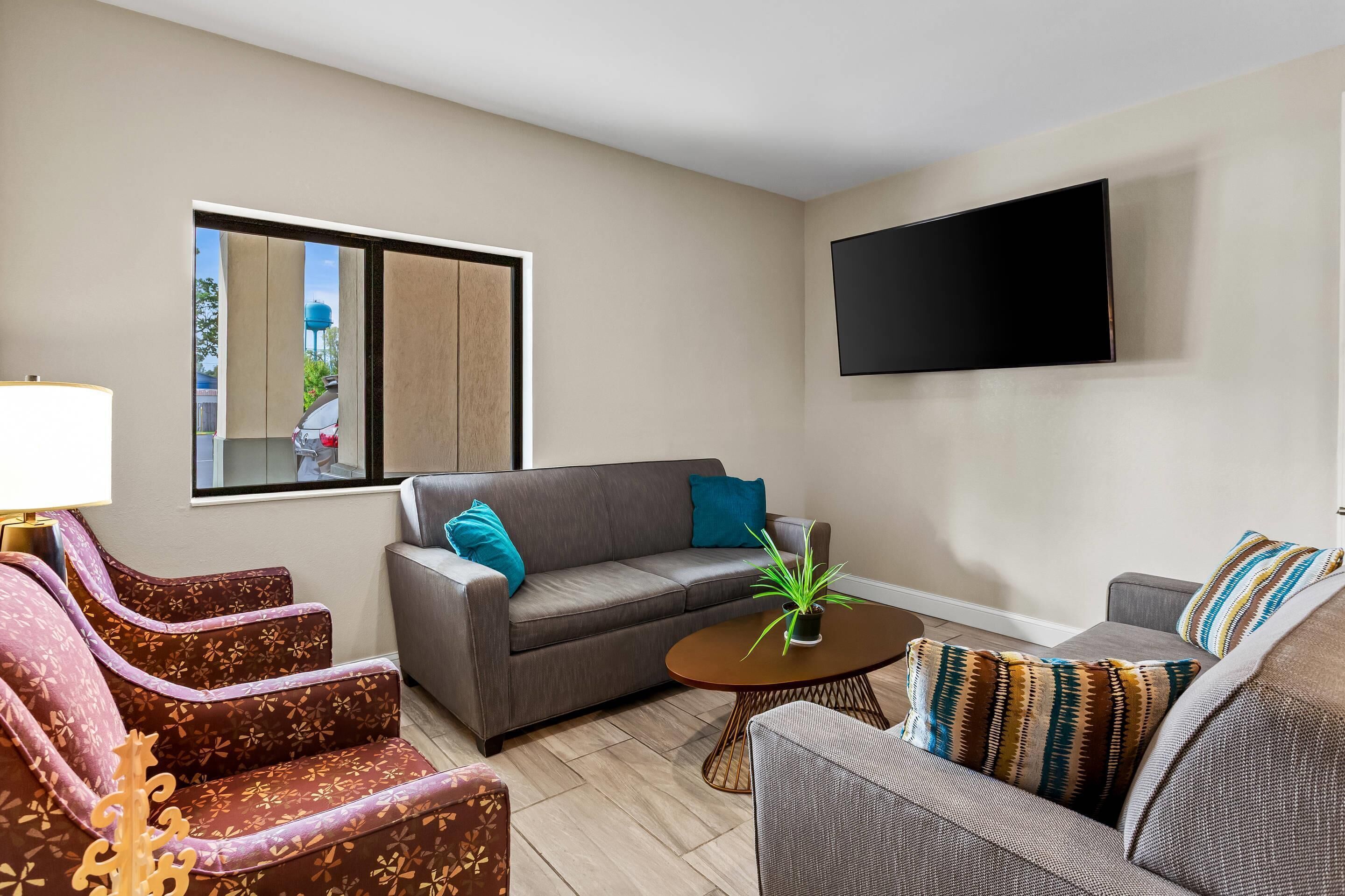Una sala de estar con un sofá gris, un sillón estampado, una mesita de centro y un televisor montado en la pared.