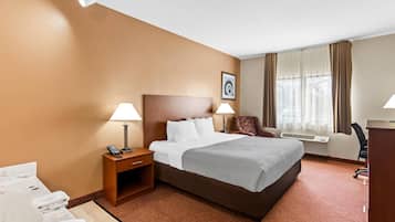 Habitación de hotel con una cama grande, dos mesitas de noche con lámparas, un escritorio con silla, una ventana con cortinas e imagen colgada en la pared.