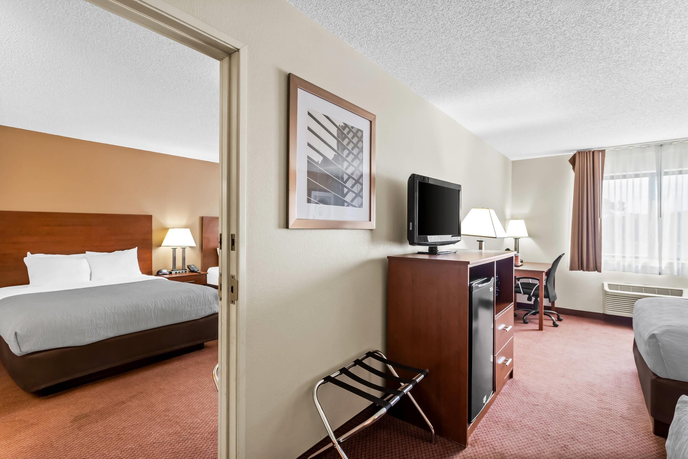Habitación de hotel con cama, escritorio, silla, televisor y ventana con cortinas.