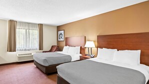 A hotel room with two beds, a desk, a chair, a lamp, and a window with curtains. - Quality Inn Sawyer (Sawyer)