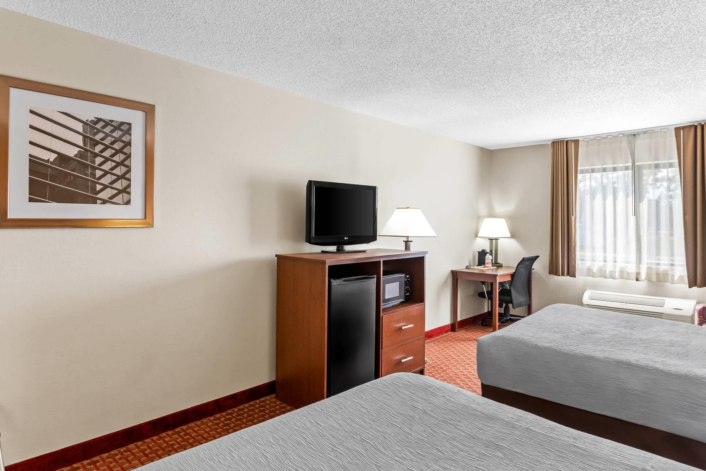 A hotel room with two beds, a desk with a computer, a television, a lamp, and a framed picture on the wall.