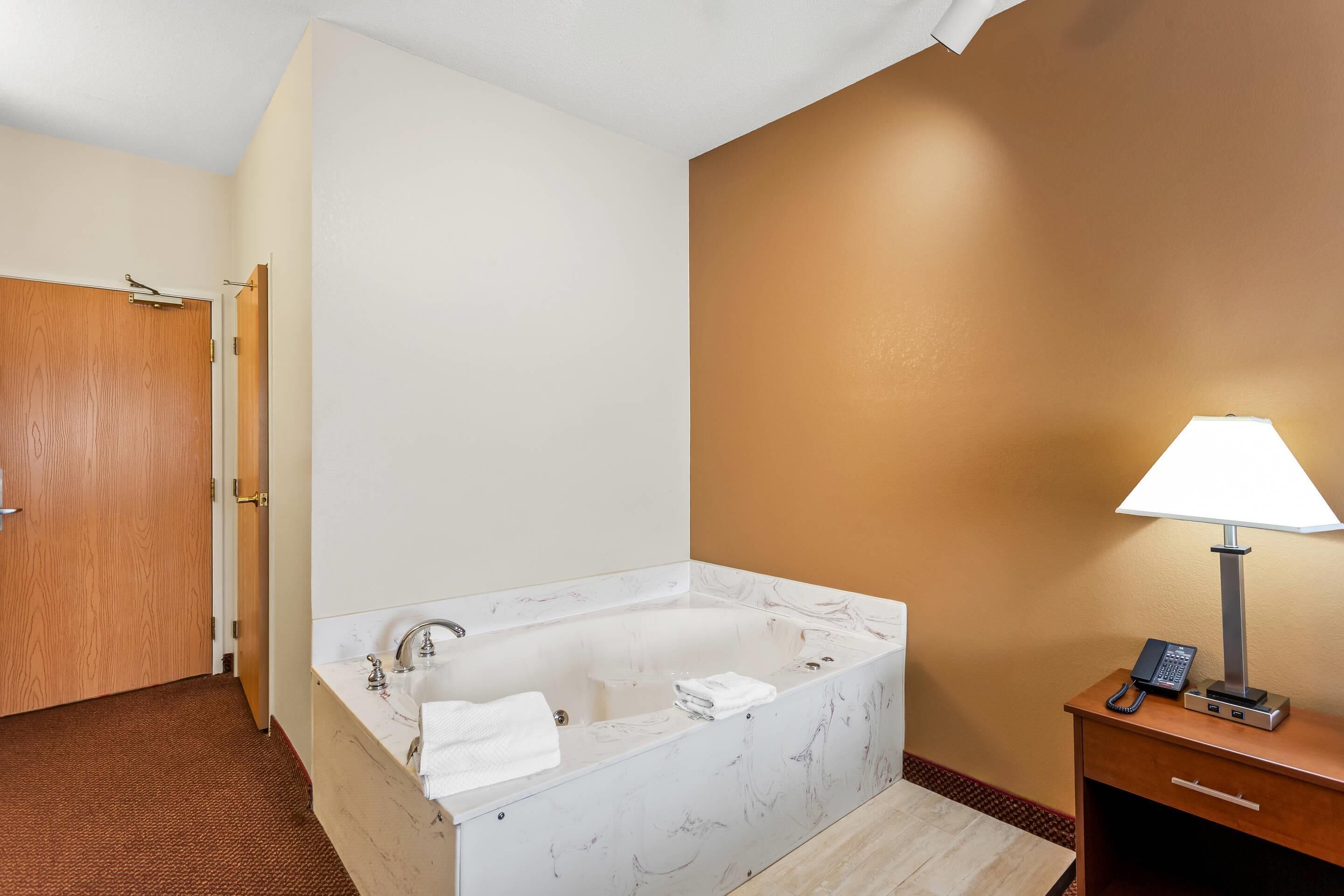 Un baño de hotel con una bañera de mármol, un lavabo, una toalla, una lámpara y un teléfono sobre una mesita de noche.
