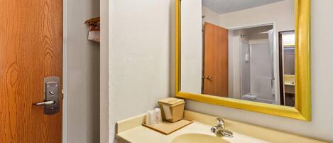 A bathroom with a wooden door, a beige sink, a mirror with a gold frame, and a towel rack.