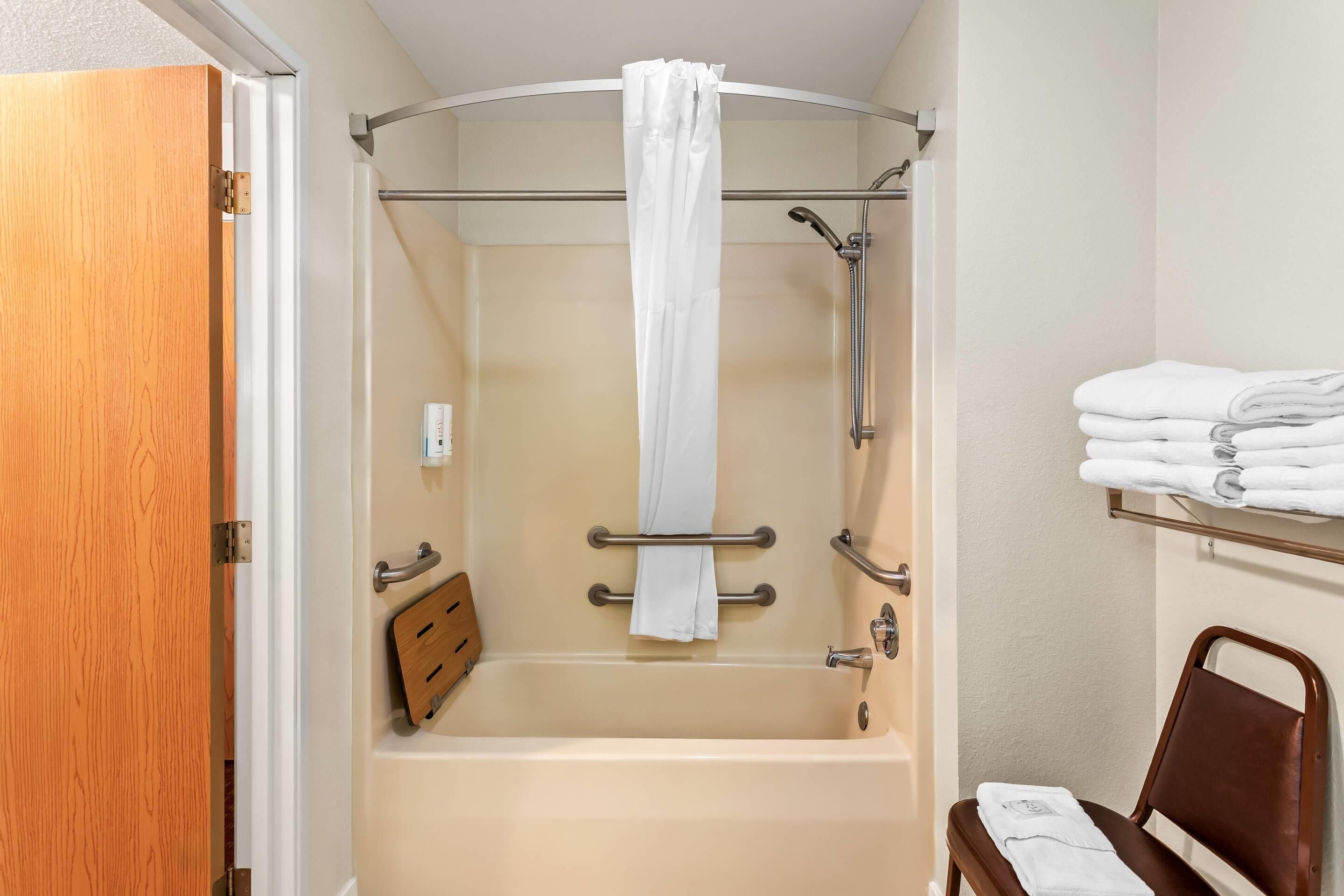 Ein Badezimmer mit Badewanne, Dusche, Handtuchhalter und einer hölzernen Sitzbank.