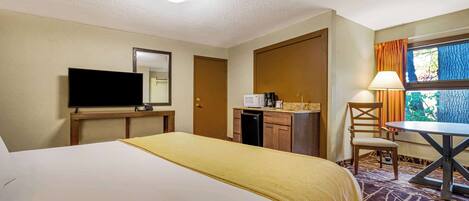 A hotel room with a large bed, a television, a microwave, a small table with a chair, and a window with curtains.