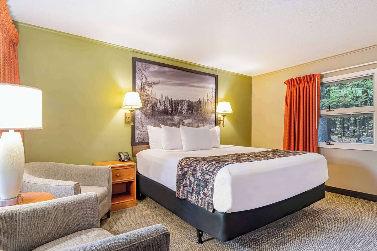 Une chambre d’hôtel avec un grand lit, deux lampes de chevet, une table de nuit, une chaise et une fenêtre avec des rideaux.