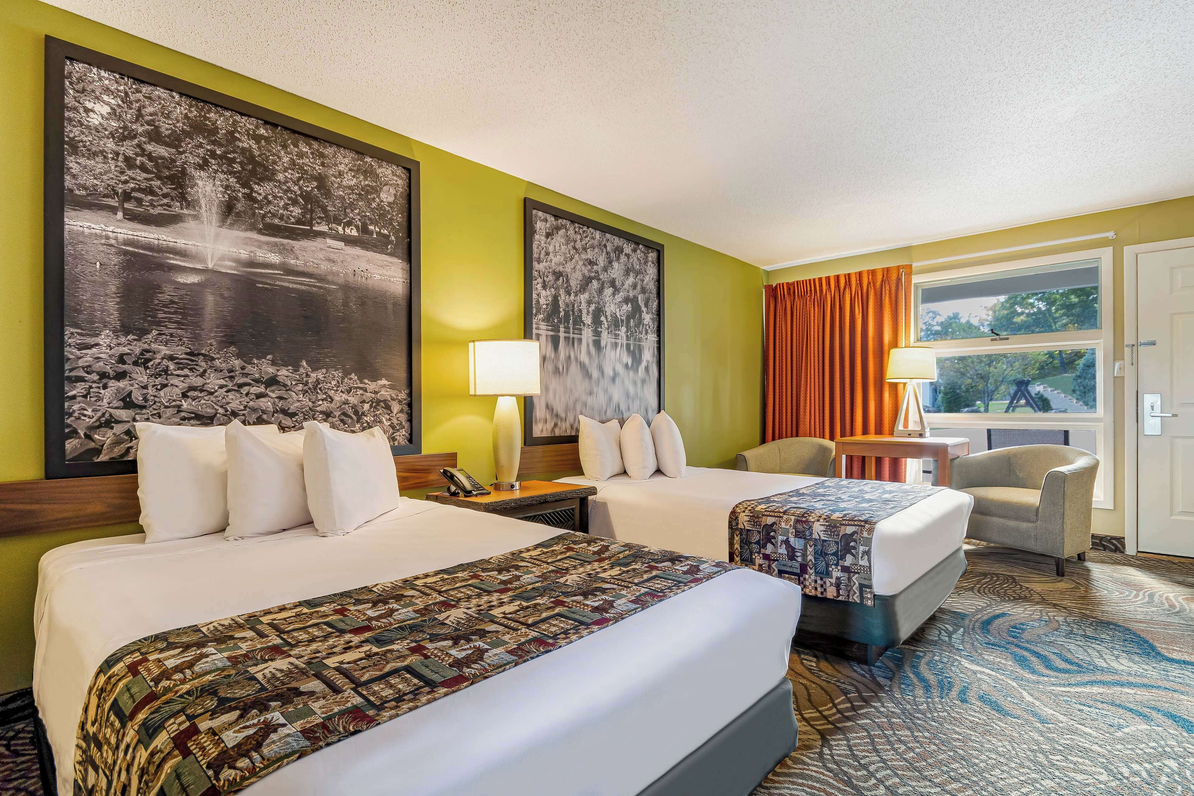 A hotel room with two beds, a large window with curtains, a chair, and two wall-mounted lamps.