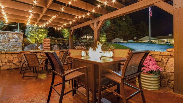 An outdoor patio with a wooden pergola, stone walls, and a fire feature.