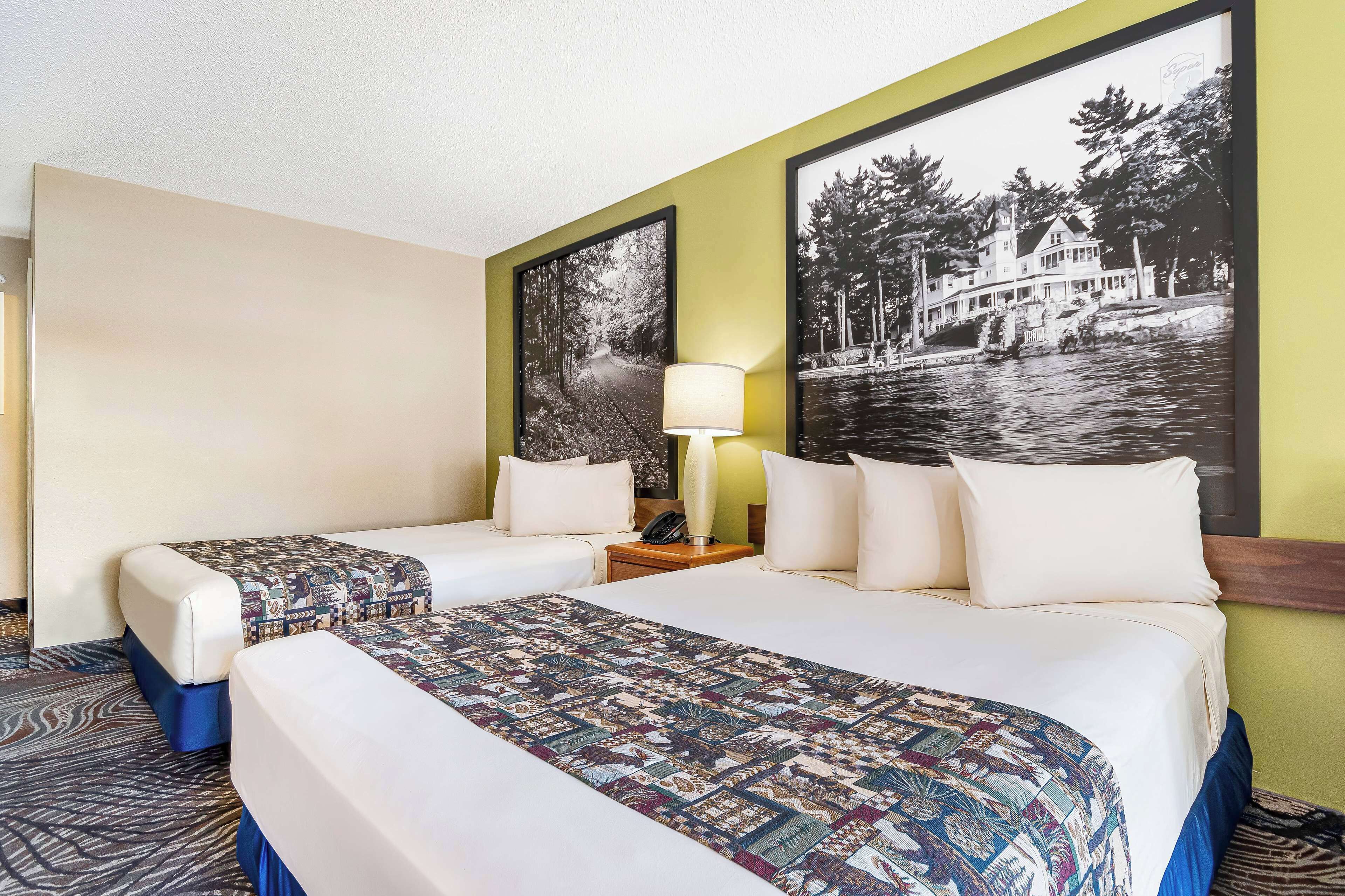 A hotel room with two beds, a patterned bedspread, a lamp, and two large black-and-white photographs on the wall.