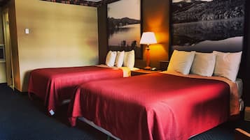 A hotel room with two beds, a nightstand, a lamp, and a painting of a mountain landscape.