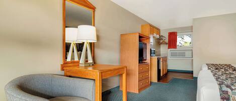 A hotel room with a wooden desk, a chair, a bed, a dresser, and a television.