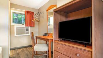Una habitación compacta con escritorio de madera, una silla, televisor sobre un mueble de madera, ventana con cortinas y un calentador fijado a la pared.
