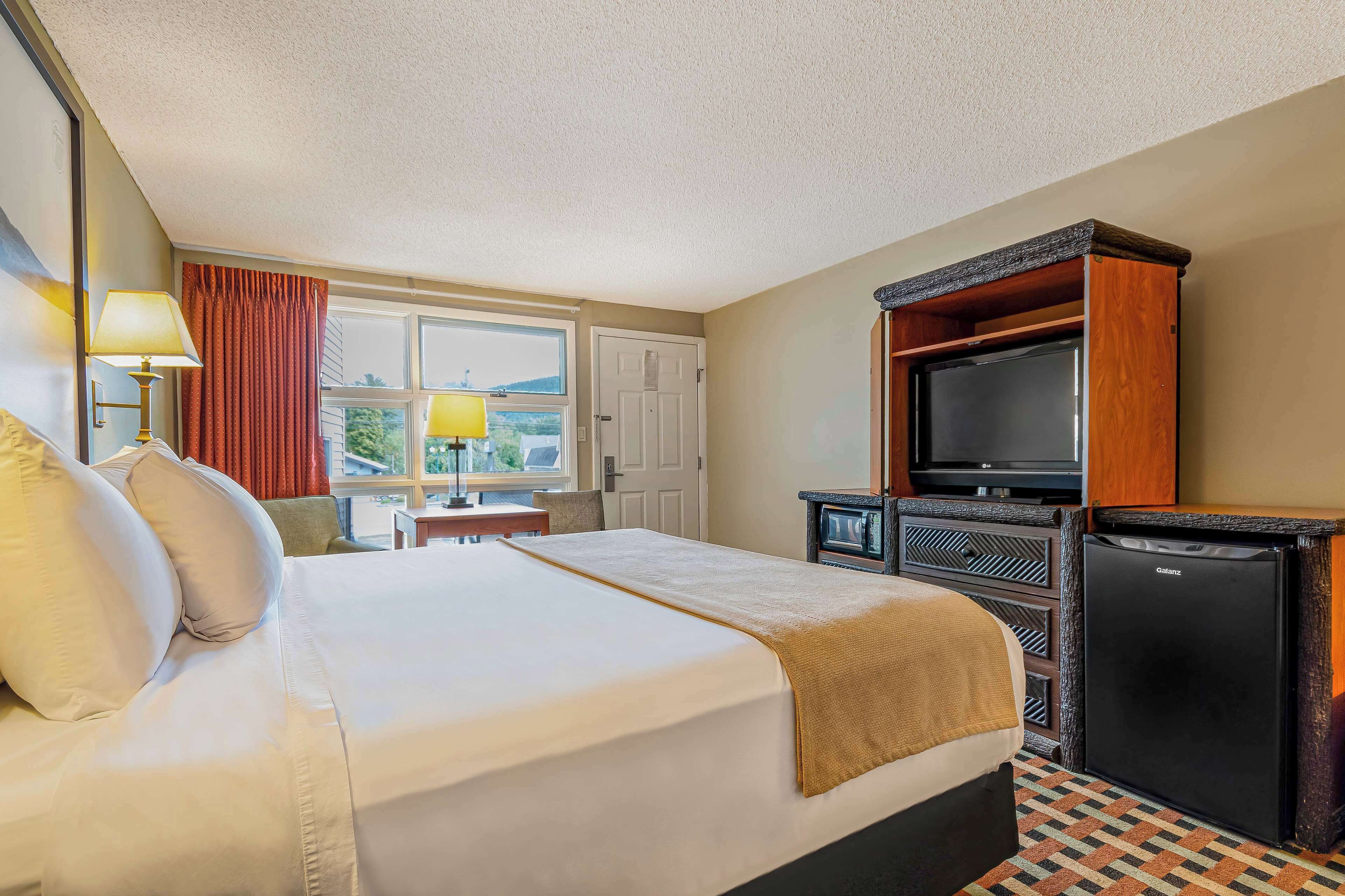 A hotel room with a bed, a television, a minibar, and a window with curtains.
