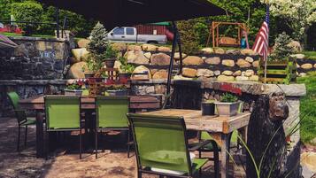 An outdoor patio with a stone wall, a wooden table, and green chairs.