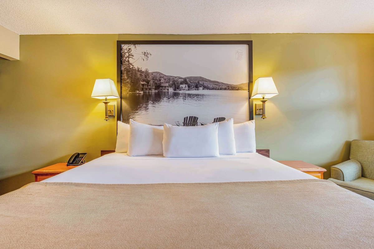 Une chambre d’hôtel avec un grand lit, deux lampes de chevet, une vue sur un lac et un fauteuil.
