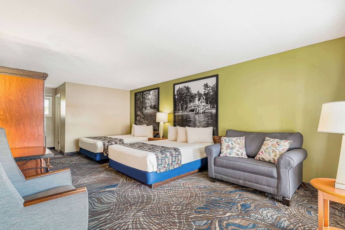 Une chambre d’hôtel avec deux lits, un canapé, un fauteuil et une moquette à motifs.