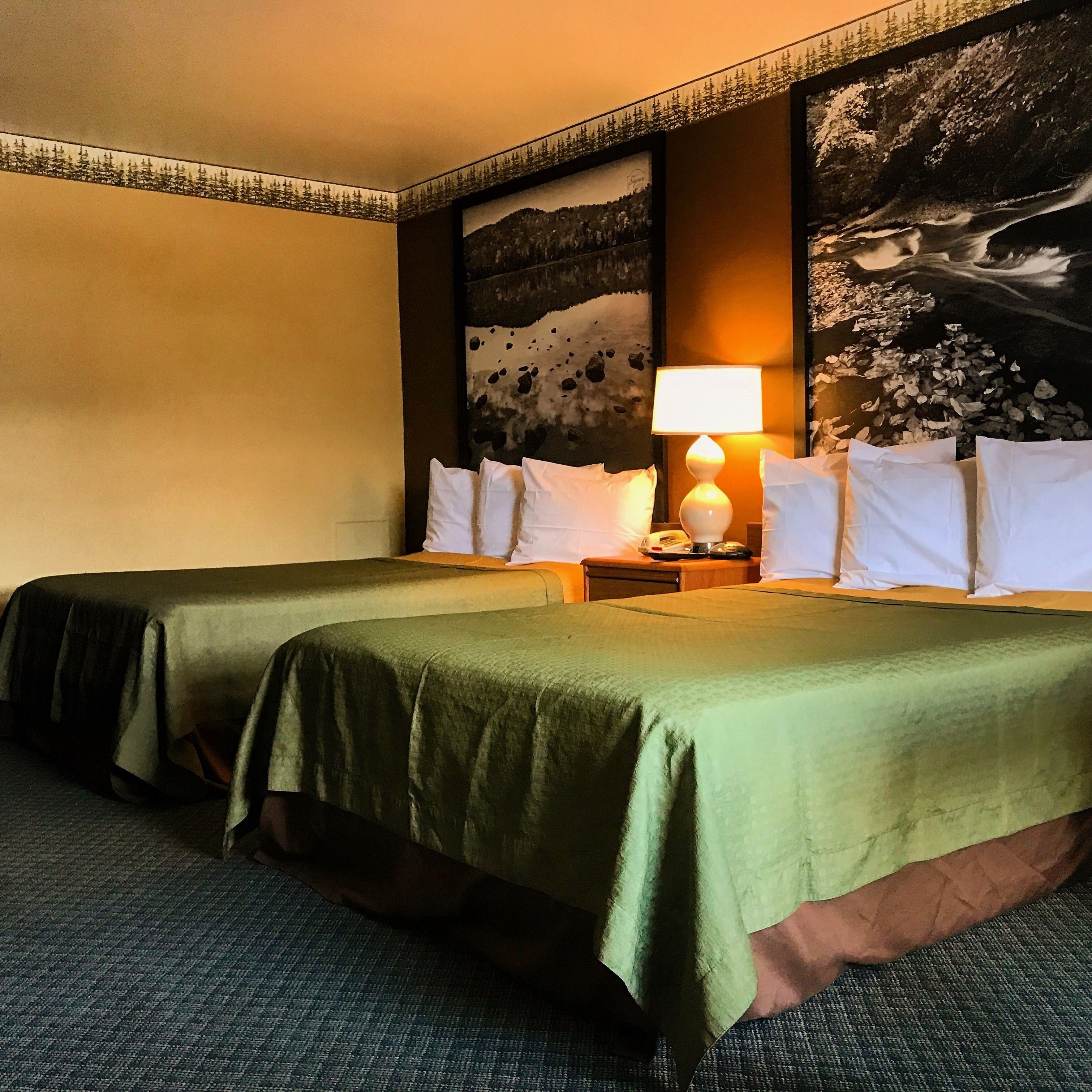 A hotel room with two beds, a nightstand with a lamp, and a large painting on the wall.