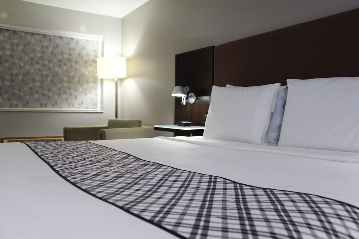 A hotel room with a large bed, a desk, a chair, a lamp, and a wall with a patterned design.
