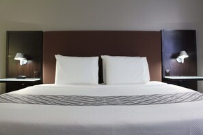 A hotel room with a large bed, two bedside tables, and wall-mounted lamps.