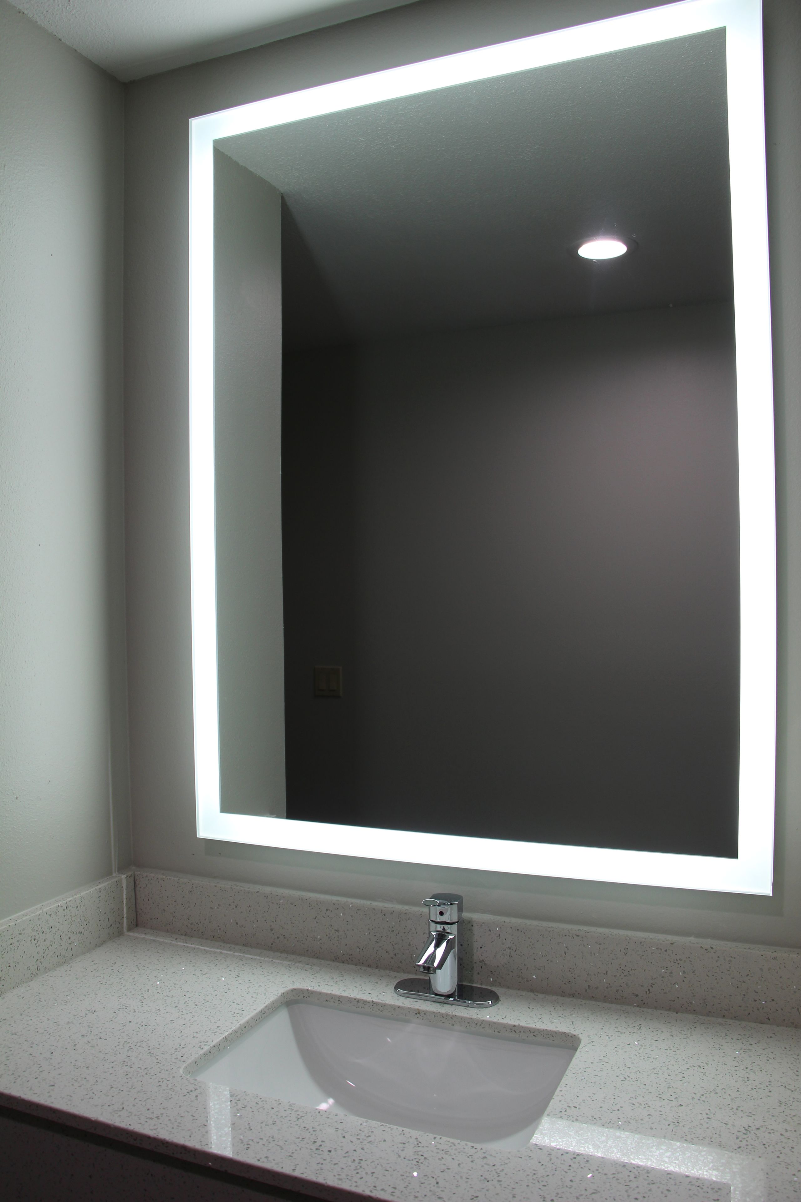 A bathroom with a white sink, a mirror, and a light fixture above the mirror.