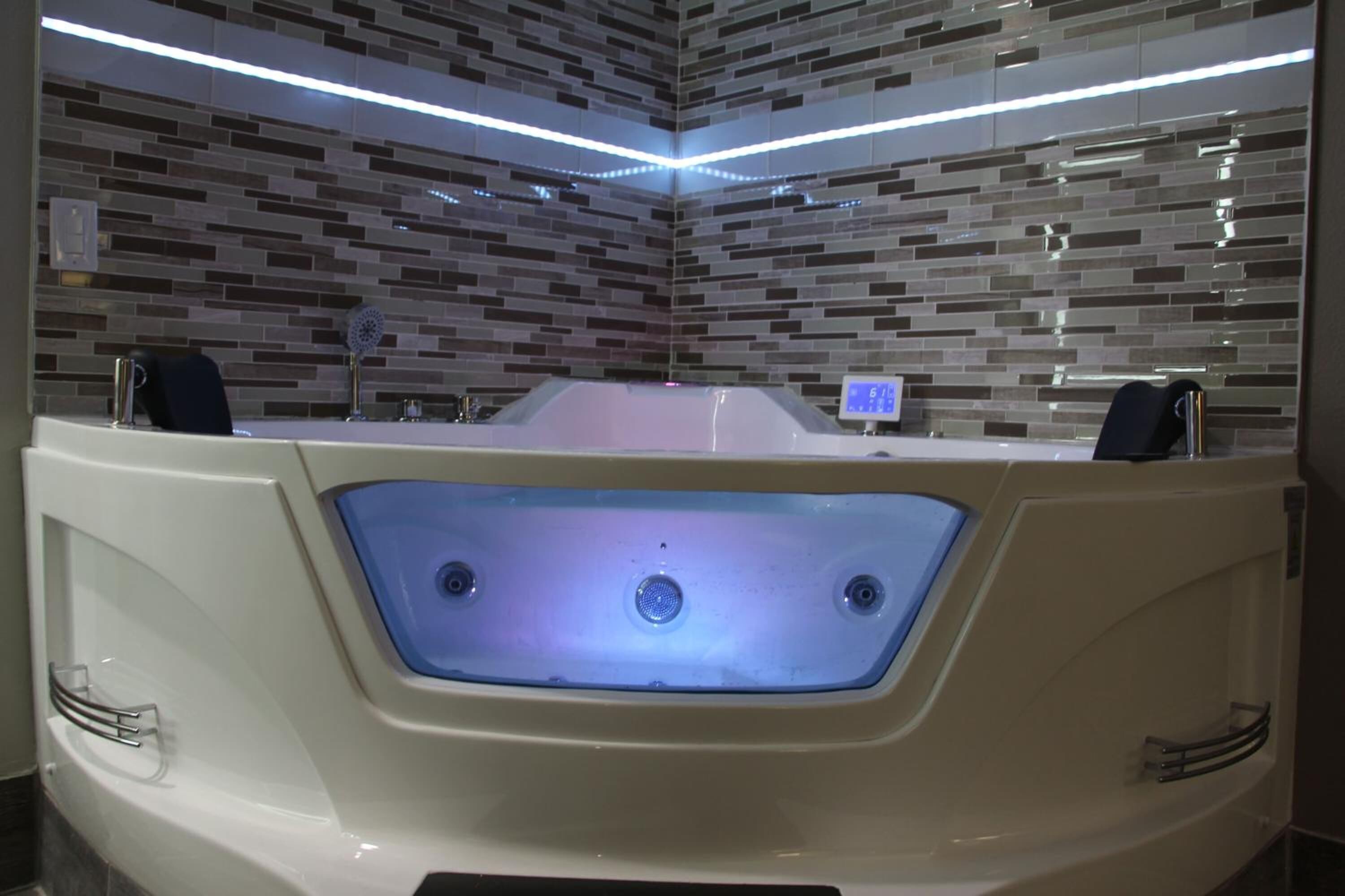 A modern bathroom with a large bathtub, a digital control panel, and a tiled wall.