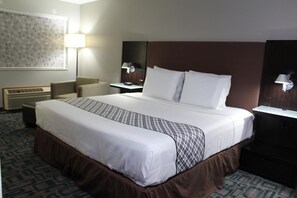 A hotel room with a large bed, a desk, a chair, a lamp, and a wall-mounted heater.
