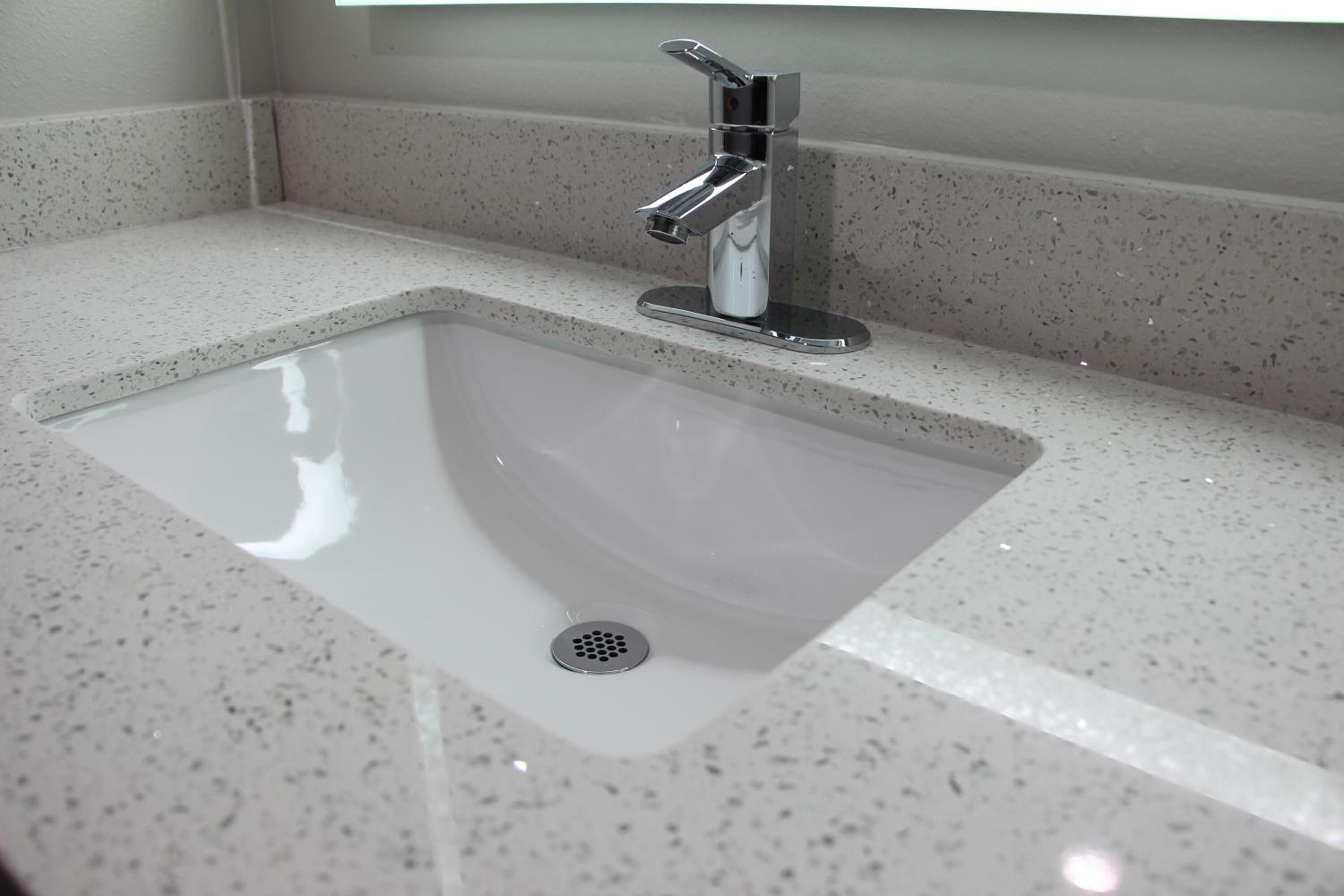Un baño moderno con un lavamanos rectangular, grifo cromado y encimera con motas.