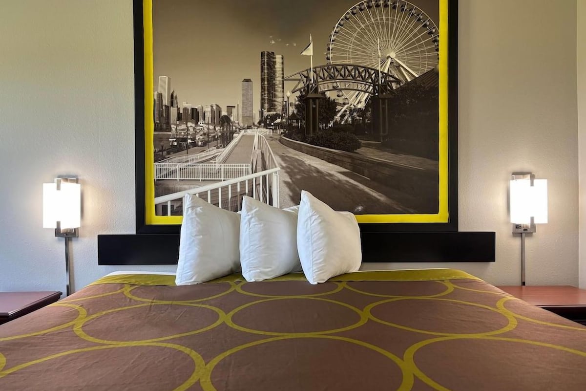 Una habitación de hotel con una cama, almohadas, cabecera y un cartel grande con vistas a la ciudad.