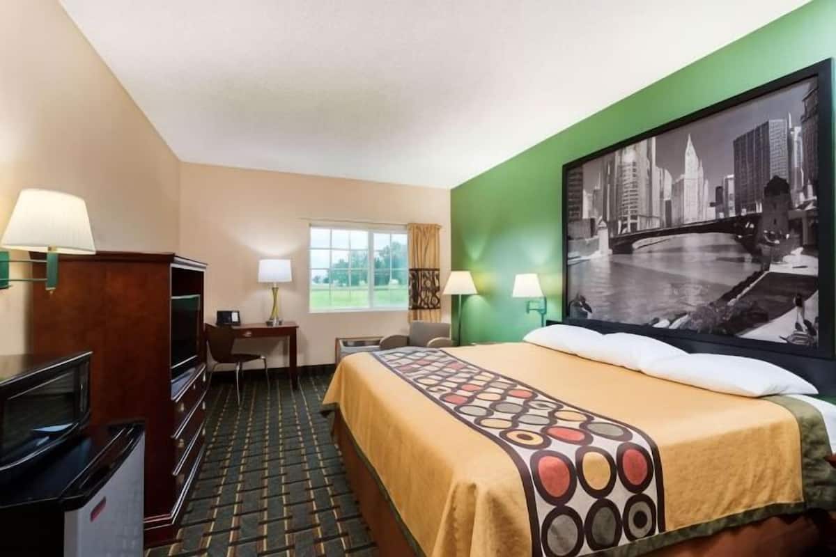 A hotel room with a bed, a desk, a television, and a large cityscape painting on the wall.