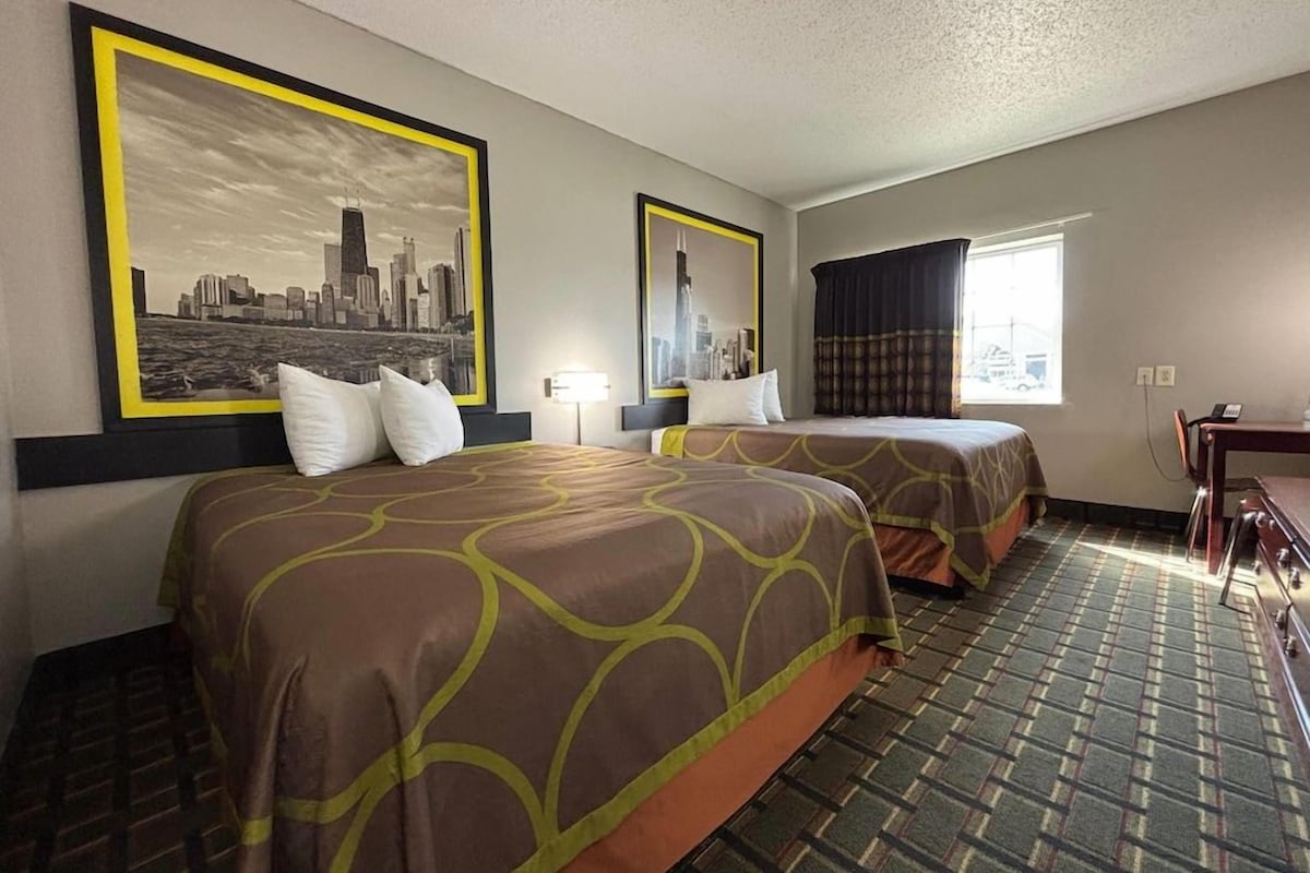 Habitación de hotel con dos camas, vista a la ciudad, alfombra estampada y un escritorio con silla.