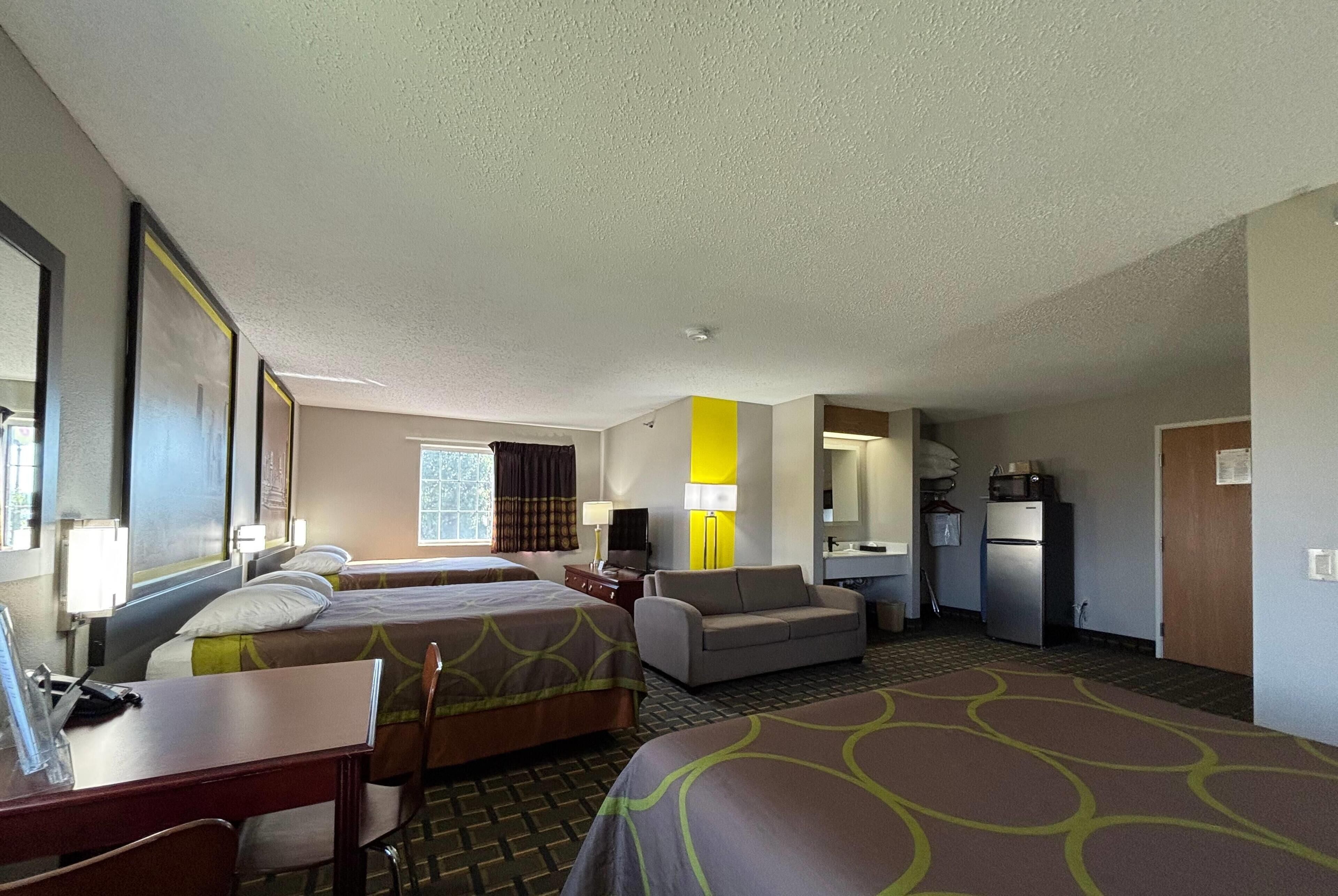A hotel room with two beds, a sofa, a desk, a lamp, a refrigerator, and a window.