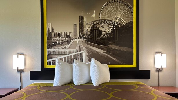 A hotel room with a bed, pillows, a headboard, and a large cityscape poster on the wall.