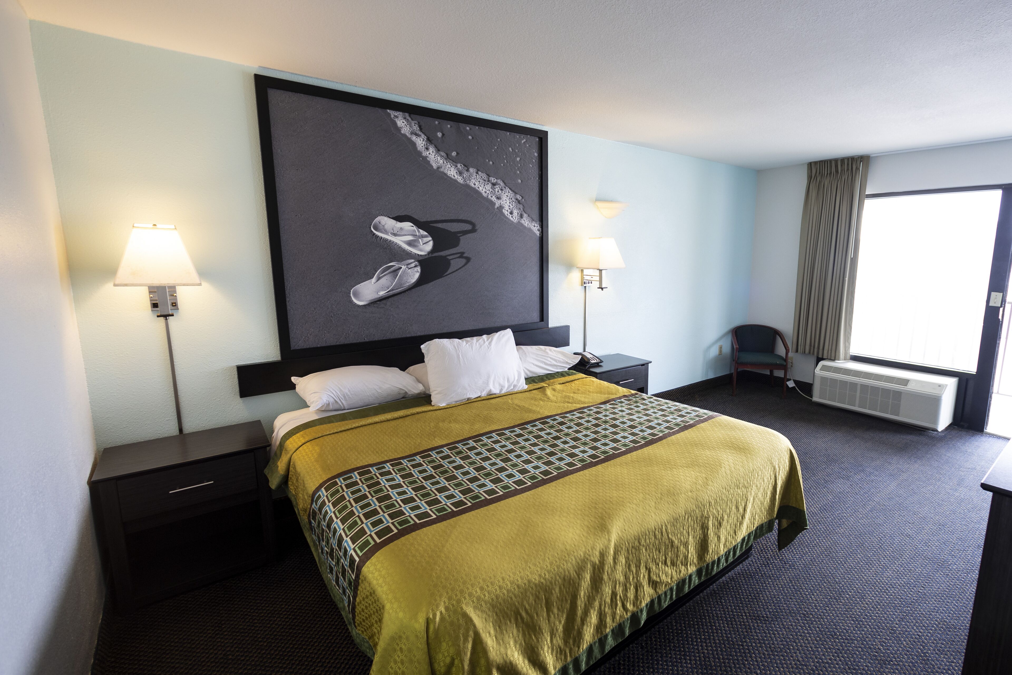 Une chambre d’hôtel avec un grand lit, deux lampes de chevet, une chaise et une grande fenêtre avec des rideaux.