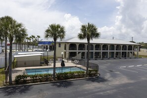 A hotel with a swimming pool, palm trees, and a parking lot.