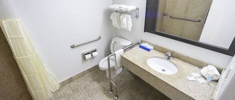 A bathroom with a sink, toilet, and handrails. There is a towel rack above the toilet and a mirror above the sink.