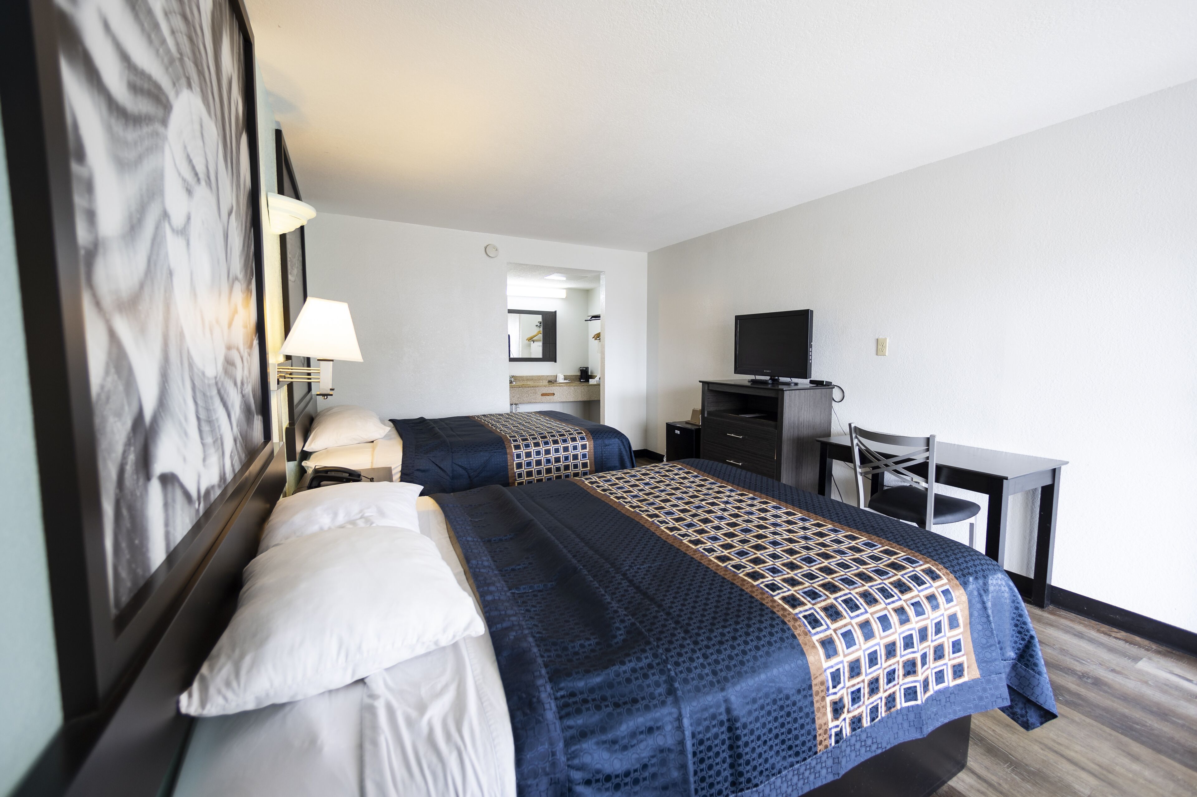 Habitación de hotel con dos camas, un escritorio, una silla, un televisor y un espejo.