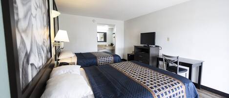 Habitación de hotel con dos camas, un escritorio, una silla, un televisor y un espejo.