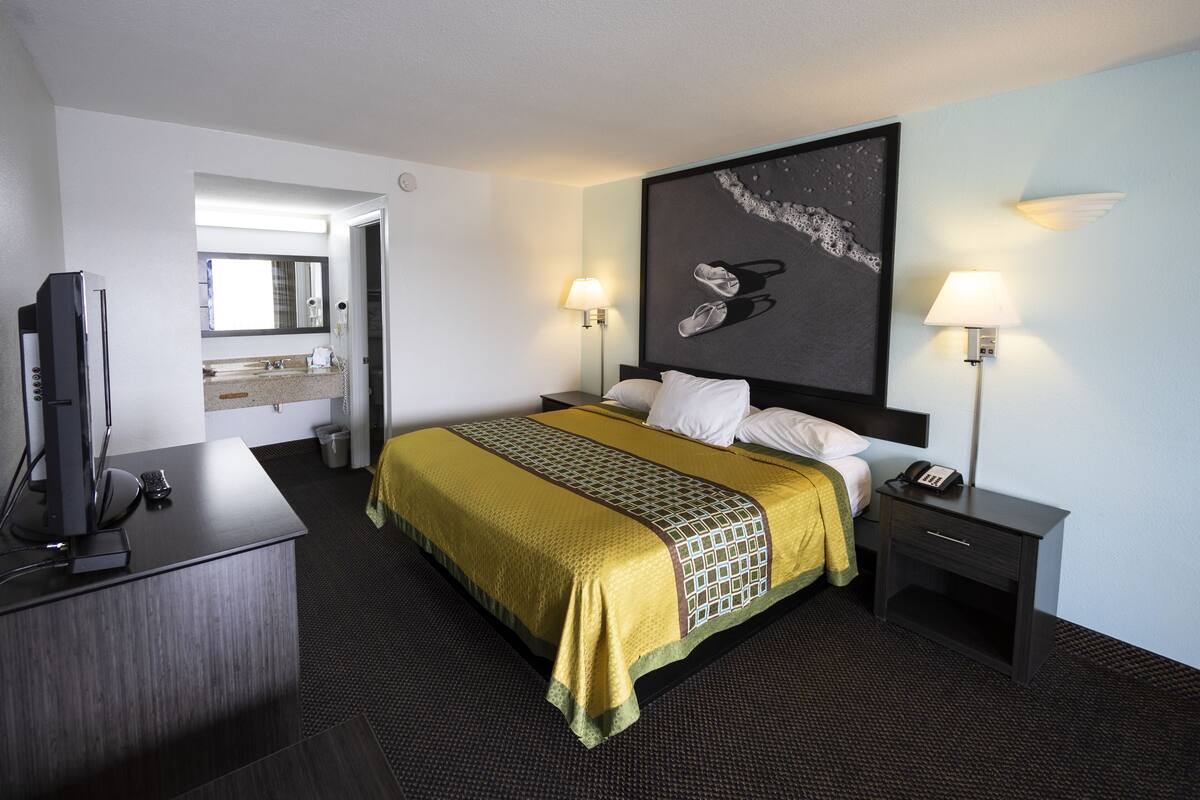 Una habitación de hotel con una cama, lámparas de noche, un escritorio con televisor y una obra de arte grande en la pared.