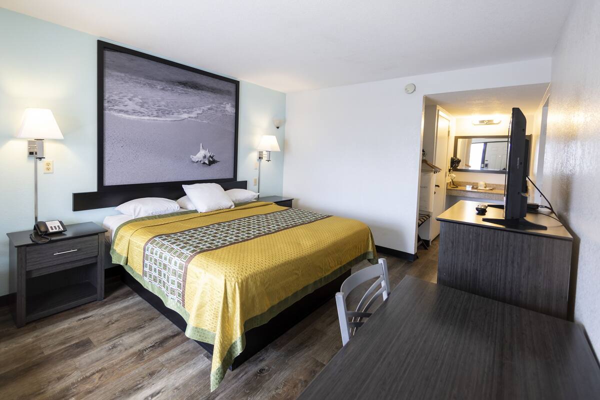 Una habitación de hotel con cama, mesitas de noche, un escritorio con silla, televisor y un baño visible a través de una puerta abierta.