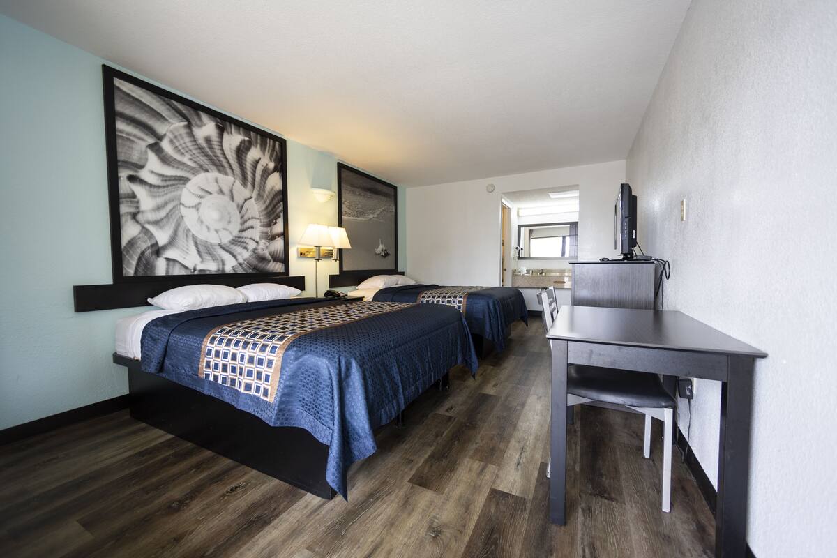 Habitación de hotel con dos camas, un escritorio, una obra de arte grande en la pared y un espejo.