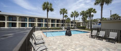 A pool area with a tiled floor, lounge chairs, and a covered seating area.