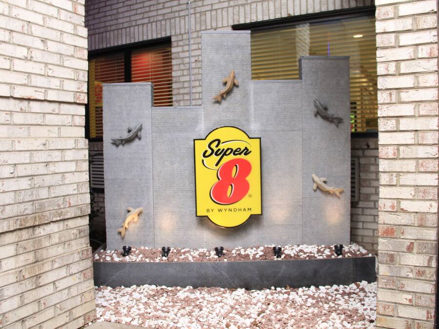 A brick building with a large sign reading "Super 8 by Wyndham" and a small outdoor seating area with pebbles.