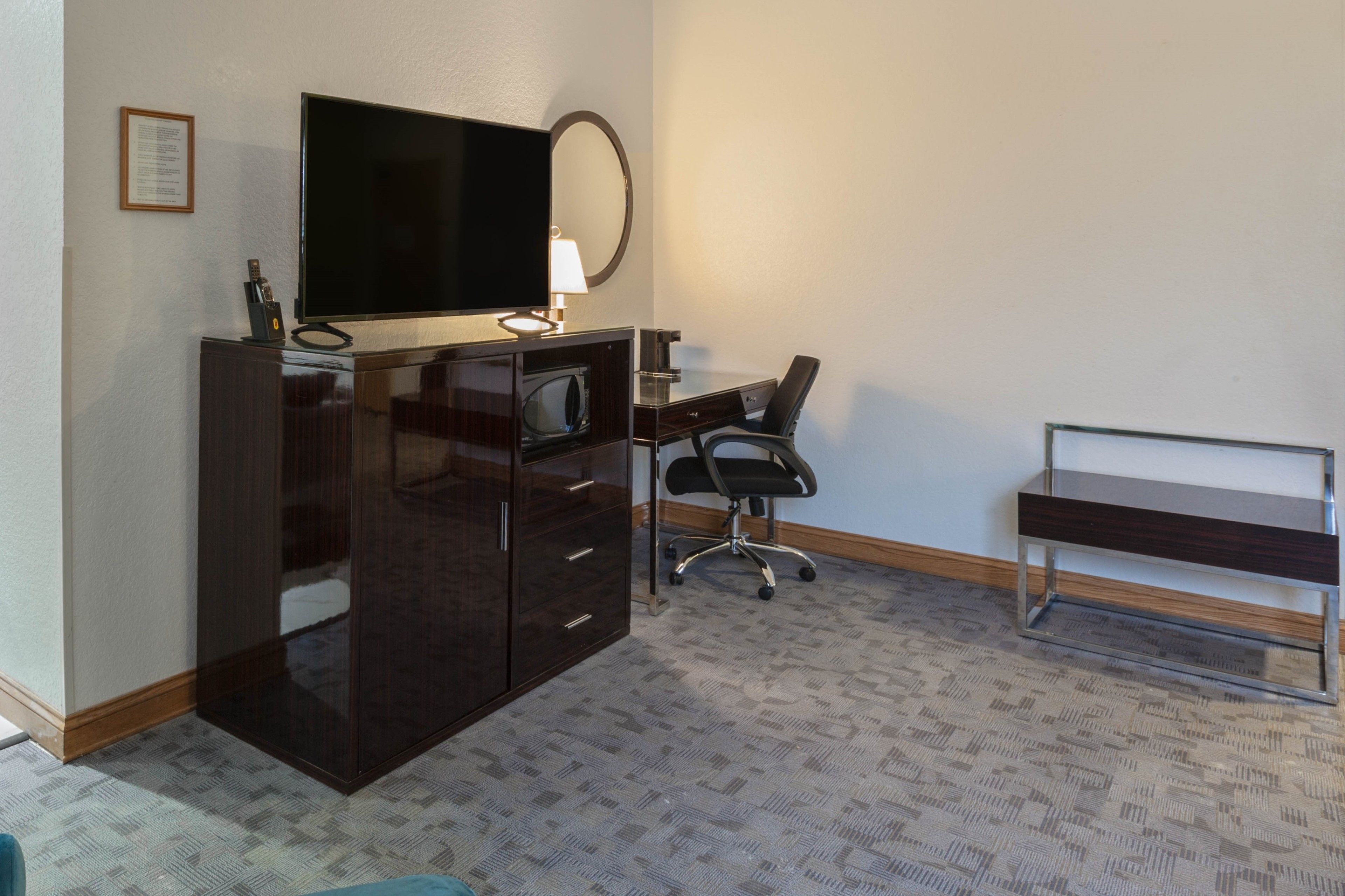 Habitación de hotel con una amplia televisión de pantalla plana, un escritorio con una silla, un espejo y una mesita.