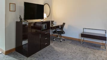 Habitación de hotel con una amplia televisión de pantalla plana, un escritorio con una silla, un espejo y una mesita.