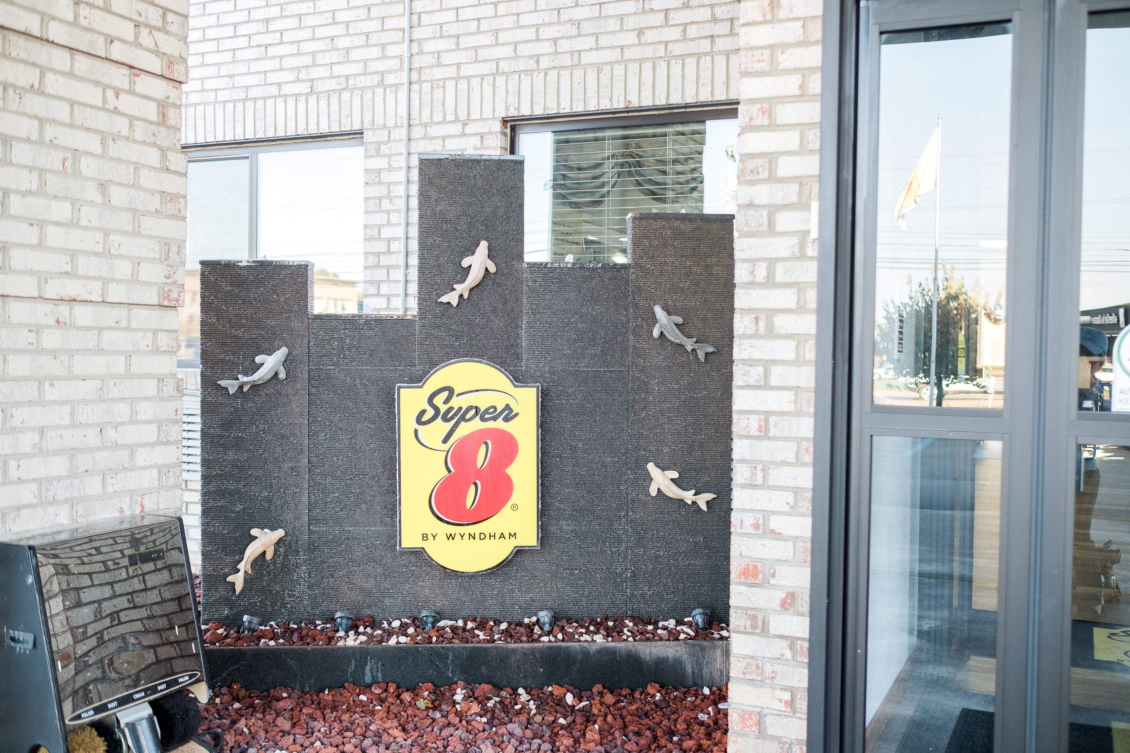 A brick building with a Super 8 By Wyndham sign, a brick wall with shark cutouts, and a window.