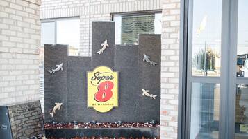A brick building with a Super 8 By Wyndham sign, a brick wall with shark cutouts, and a window.